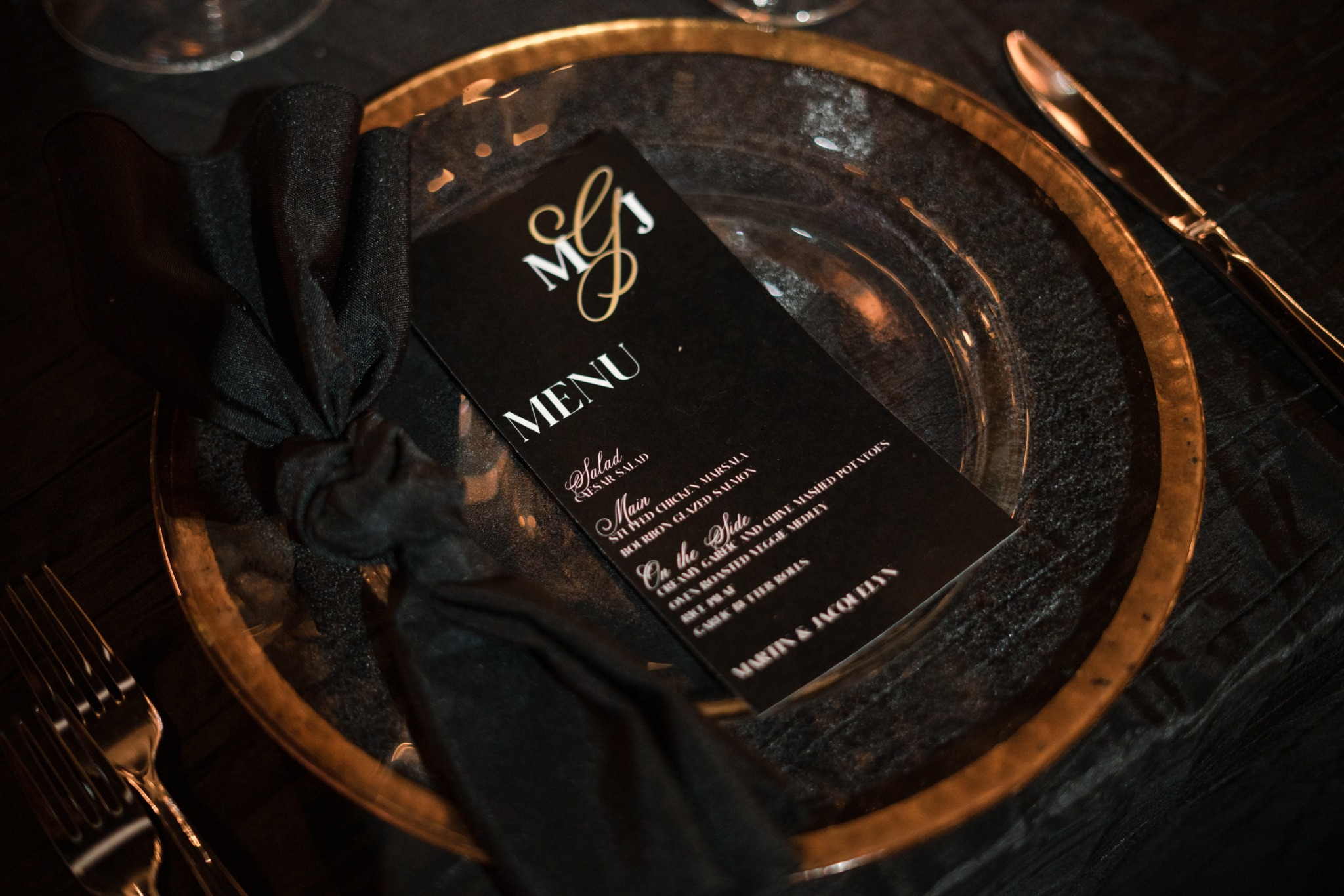 A black personalized menu and knotted napkin on a gold-rimmed glass charger