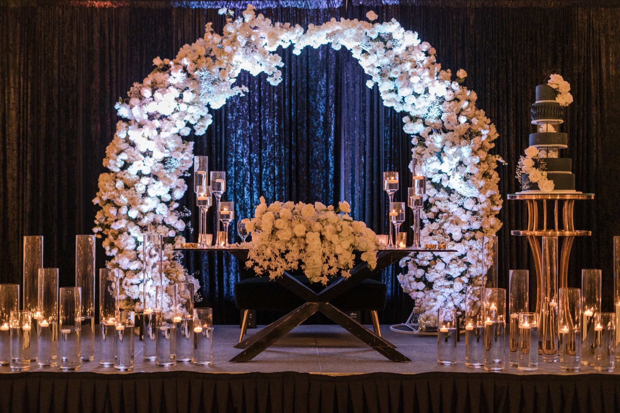White flowers framing a sweetheart table with black draping and layered candlelight