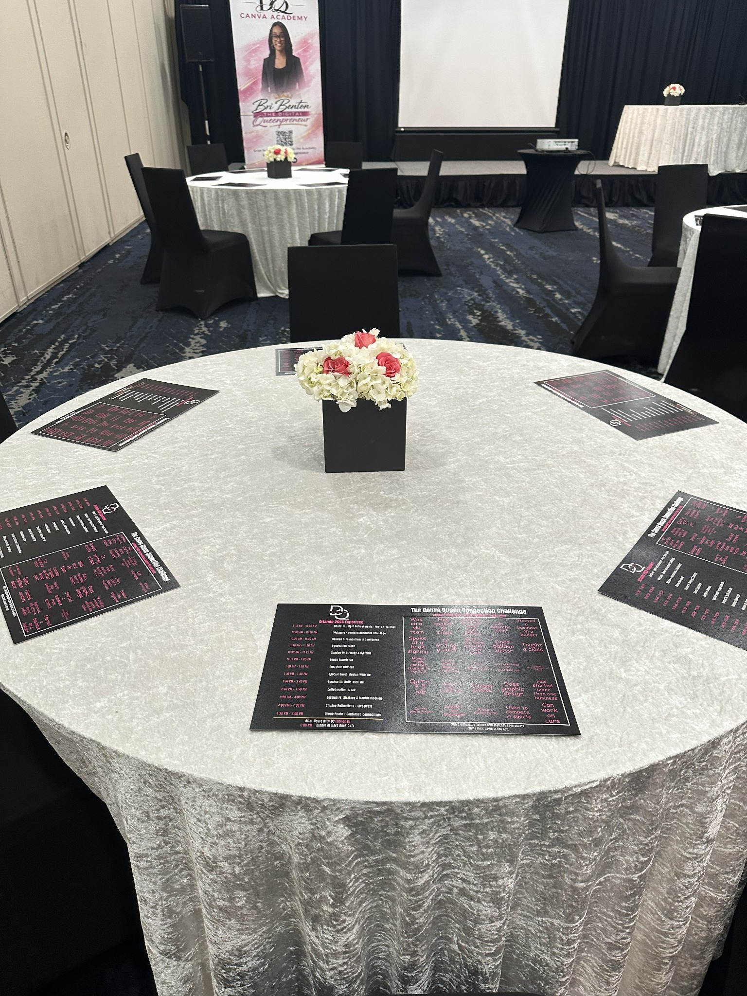 Custom printed schedules and attendee bingo cards arranged around a white velvet table with pink and ivory flowers