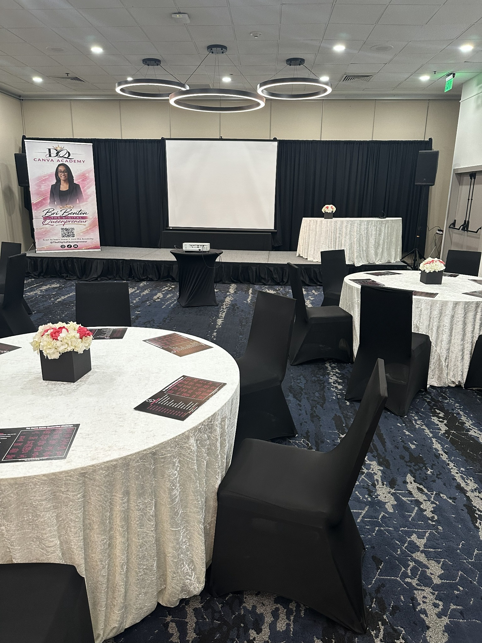 An Orlando professional meetup with a presentation stage, white velvet tables, black chairs and printed schedules at each place